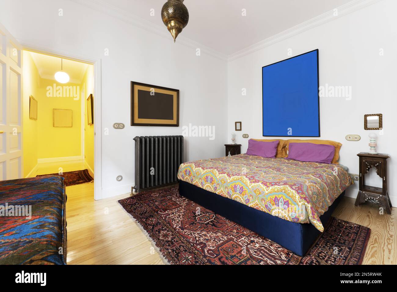 Chambre avec lit double décorée de couettes colorées et de tapis sur parquet en pin Banque D'Images