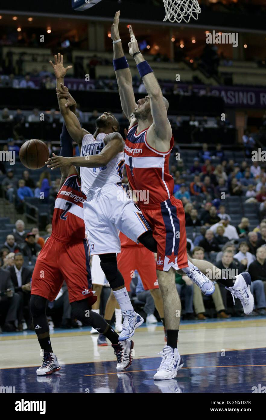 Charlotte Bobcats' Kemba Walker, center, is fouled driving between Washington Wizards' Marcin Gortat, right, and John Wall, left, during the first half of an NBA basketball game in Charlotte, N.C., Tuesday, Jan. 7, 2014. (AP Photo/Chuck Burton) Banque D'Images