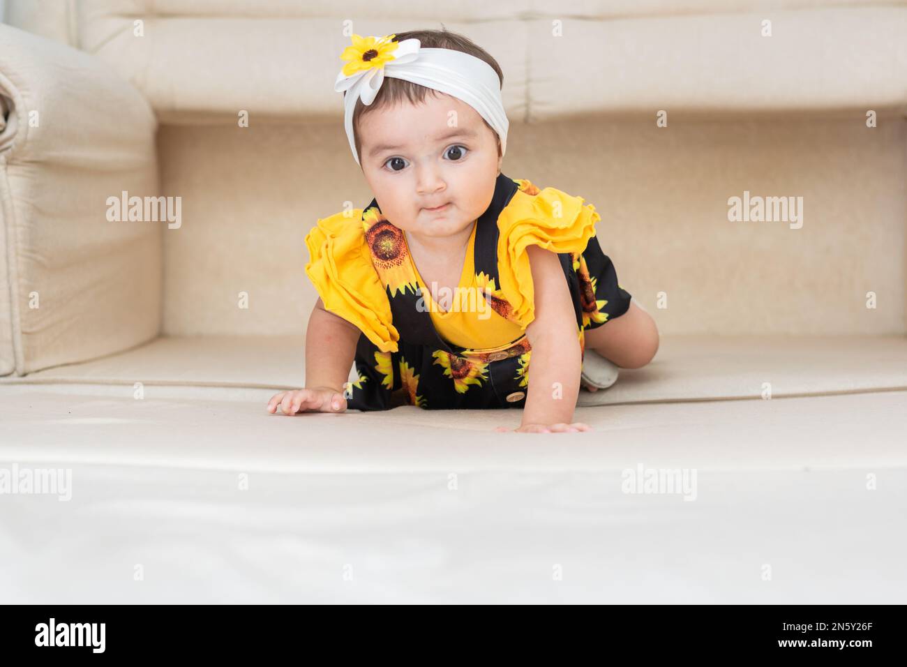bébé latina, apprendre à ramper, sur le dessus du canapé avec un visage effrayé Banque D'Images