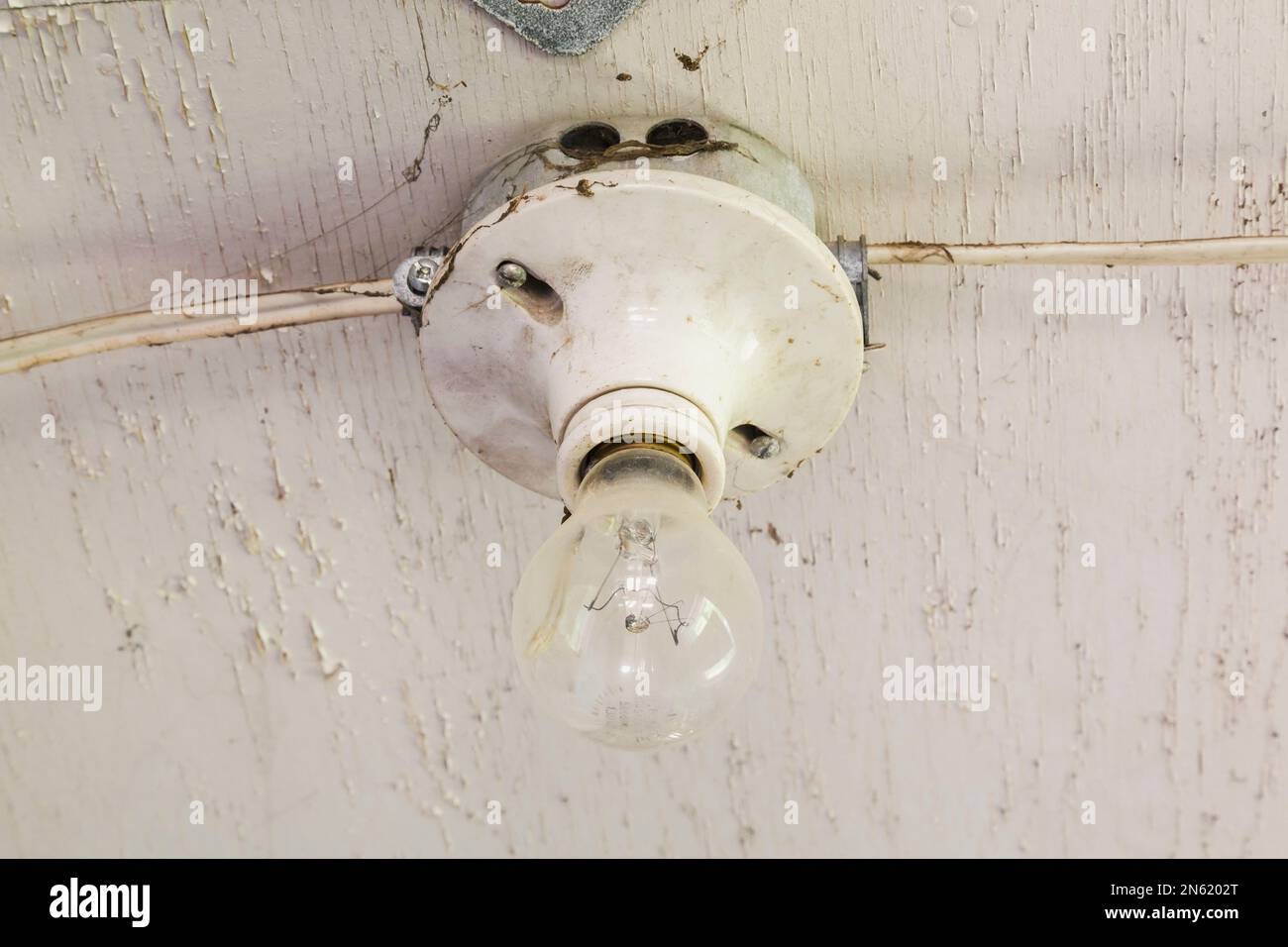 Gros plan d'une ampoule et d'un plafond en bois peint en blanc pâle à l'intérieur d'une ancienne grange aux intempéries. Banque D'Images