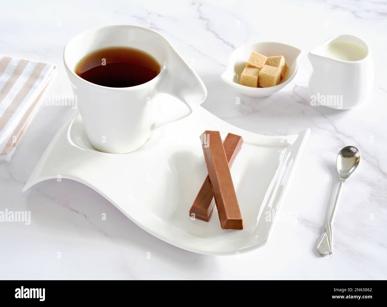 Biscuits de cachets au chocolat et thé noir en porcelaine blanche avec lait et sucre sur fond de marbre en format horizontal. Banque D'Images