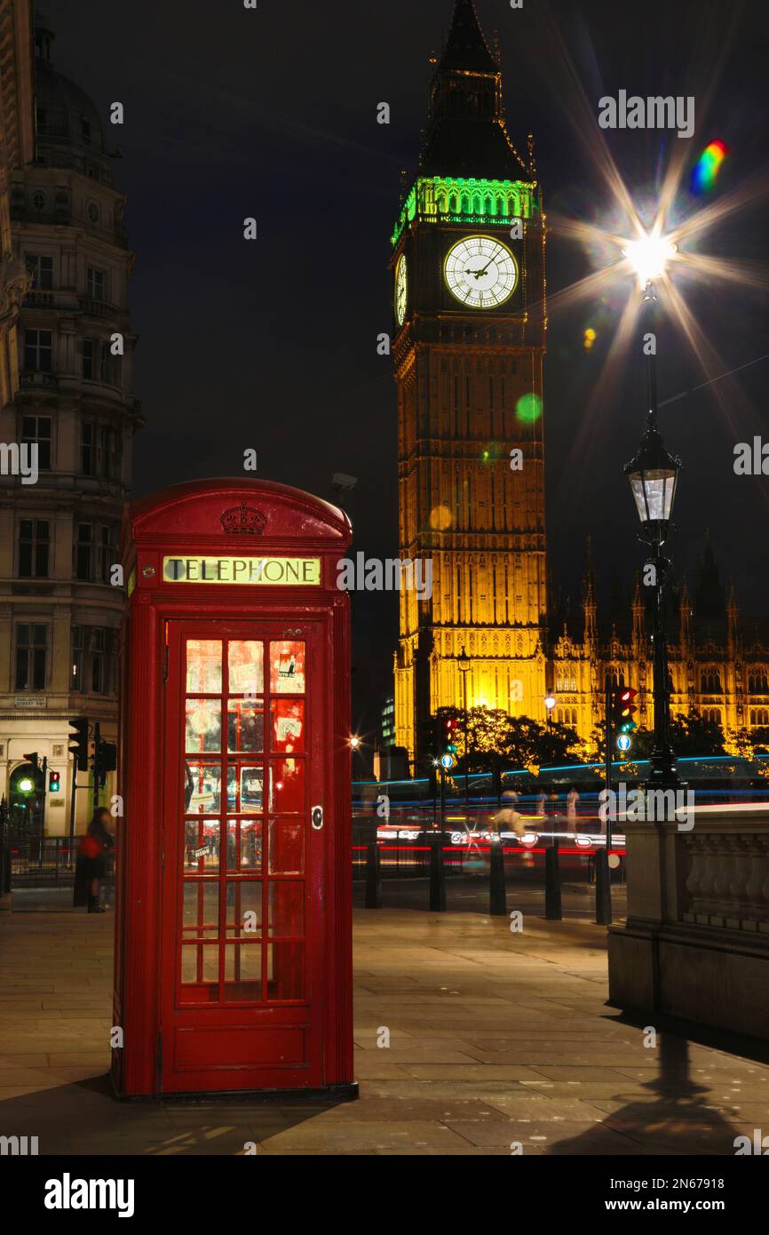 Une cabine téléphonique rouge solitaire surplombe la Tour de l'horloge de Big Ben lors d'une soirée tranquille à Londres. Il y a des voitures striées sur le châssis. Banque D'Images