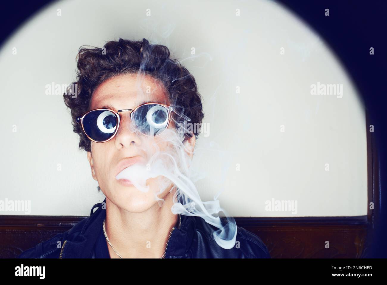 La vie vivait en excès. Portrait d'un jeune homme portant des lunettes et exhalant la fumée de cigarette. Banque D'Images