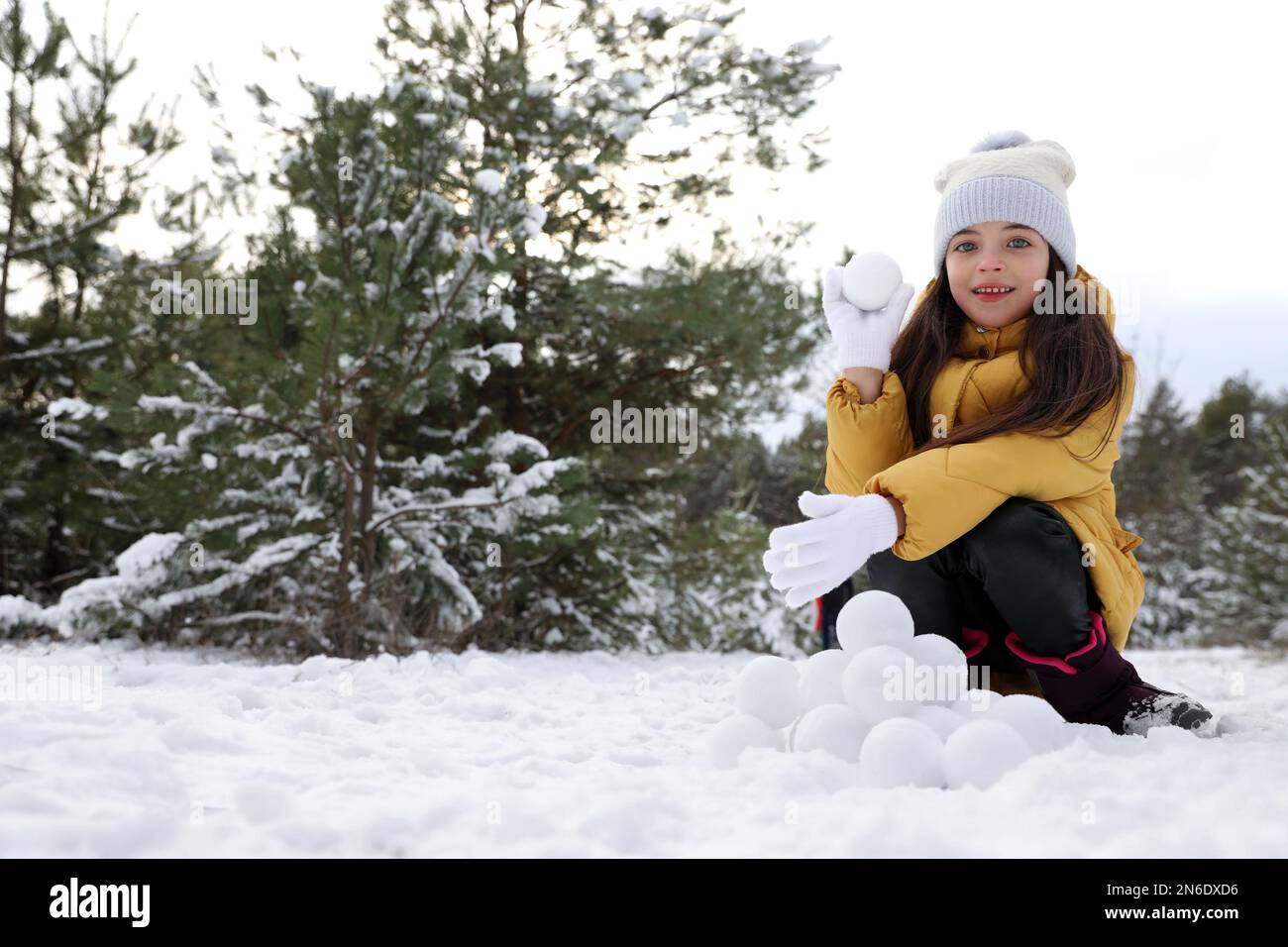 Jolie petite fille qui roule des boules de neige dans la forêt d'hiver Banque D'Images