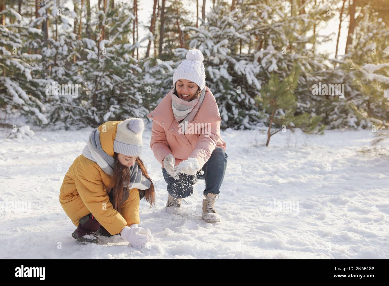 Mère et fille qui roulent des boules de neige en forêt d'hiver Banque D'Images