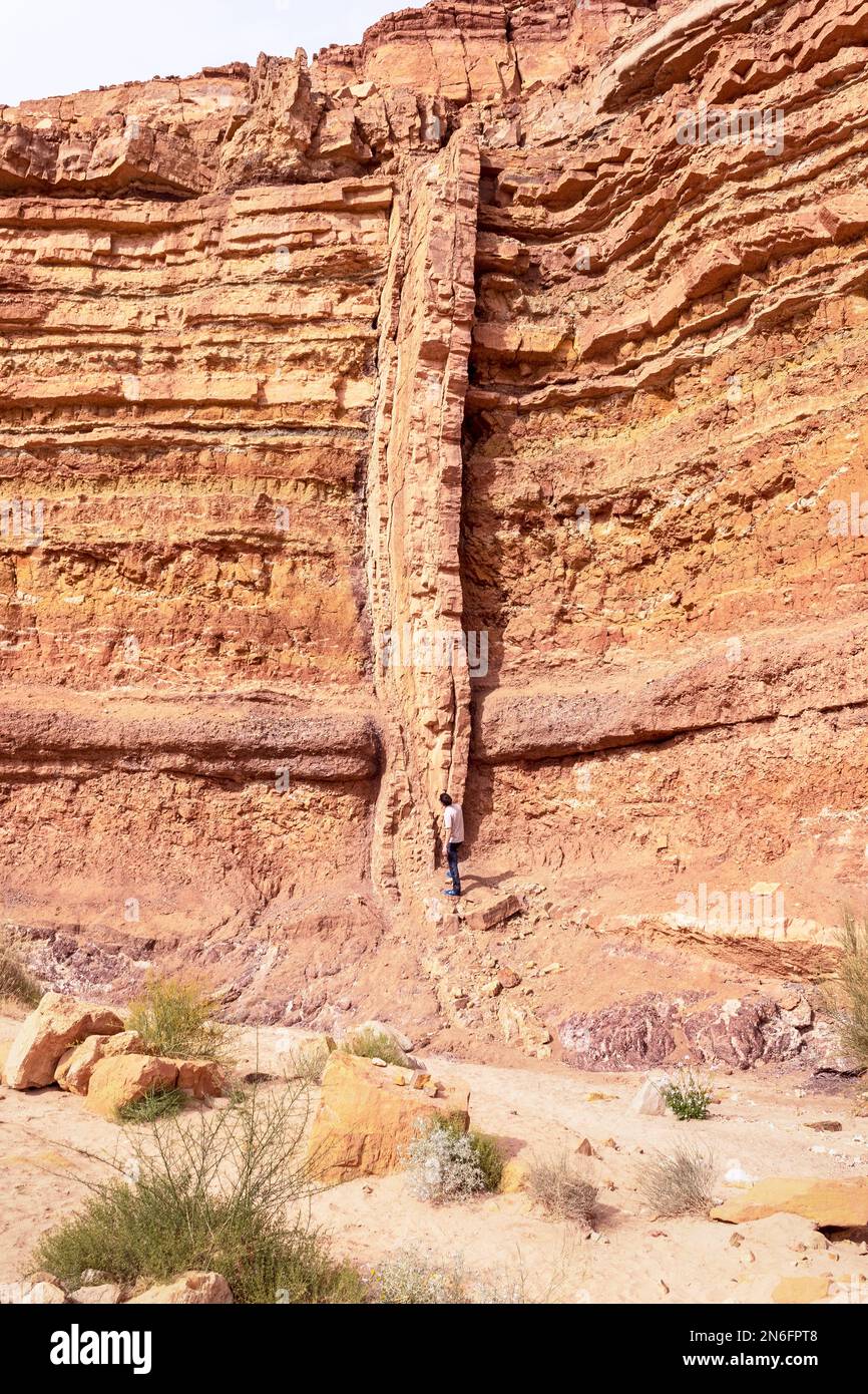 Une longue grande digue ignée magmatique verticale traverse des couches horizontales rouges et orange de roche sédimentaire dans le lit de Nahal Ardon à Makhtesh Banque D'Images
