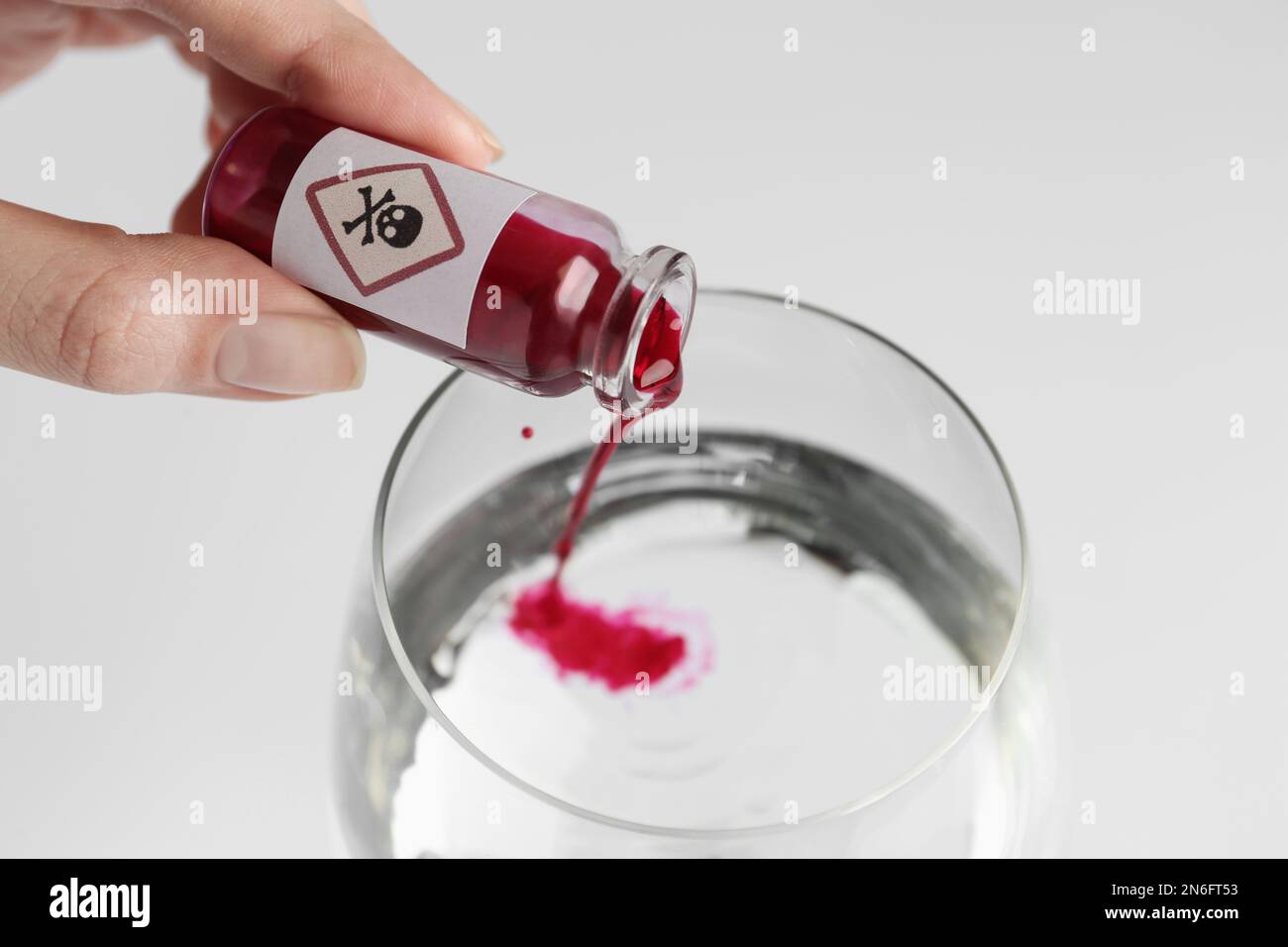 Femme versant du poison dans un verre d'eau sur fond blanc, gros plan Banque D'Images