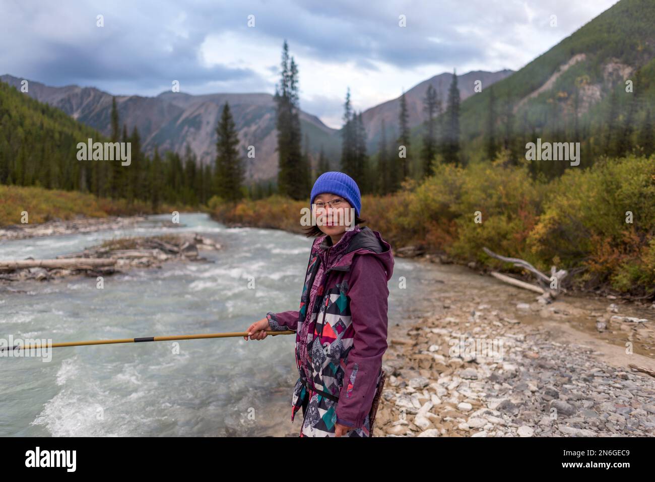 Une jeune pêcheur se tient sur les rives de la rivière alpine Shavla et attrape des poissons dans les montagnes de l'Altaï sous les nuages pluvieux près d'une forêt en Sibérie. Banque D'Images