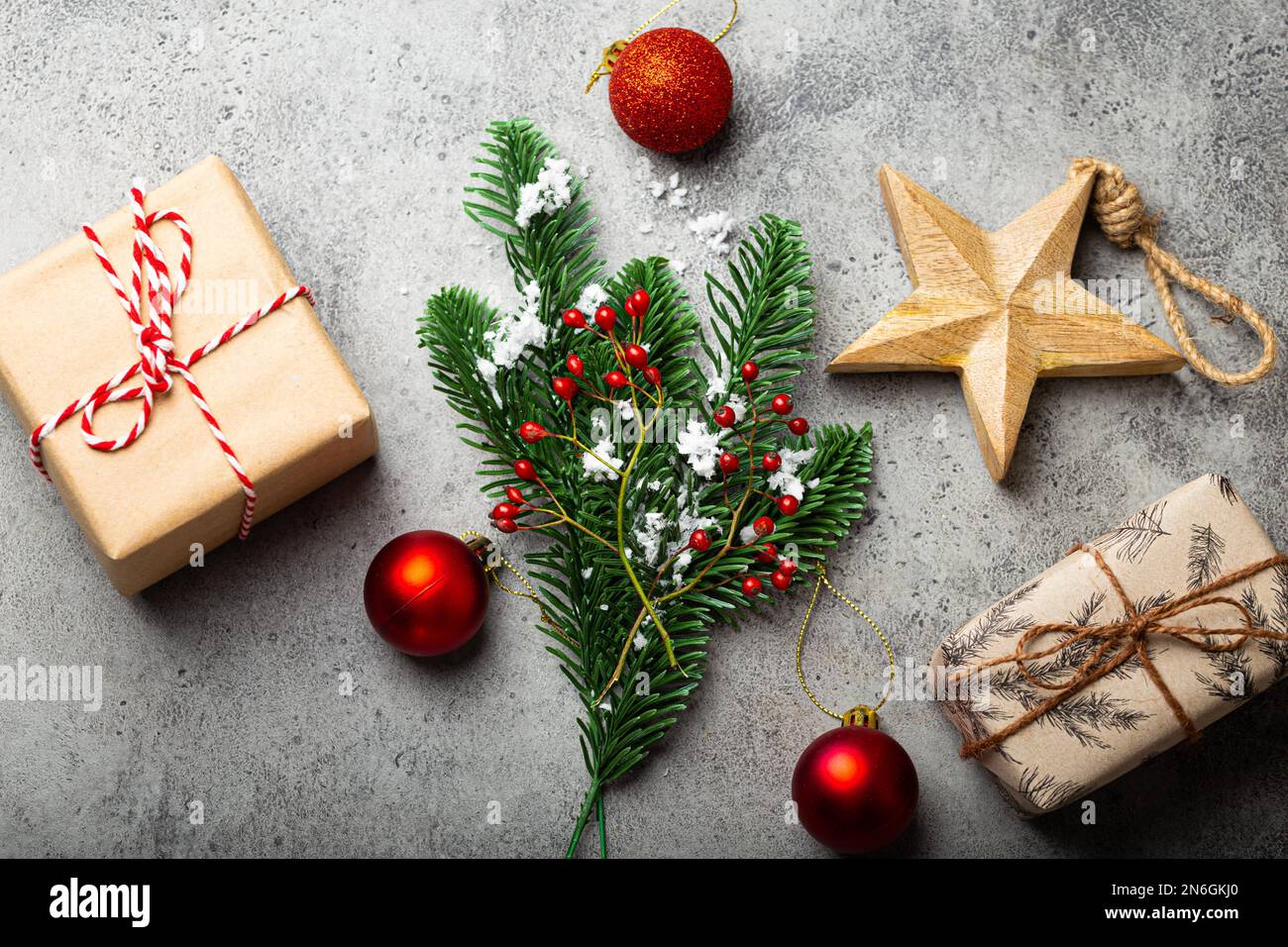 Composition de Noël et du nouvel an avec branche de sapin vert dans la neige, baies rouges, décorations de Noël et cadeaux enveloppés sur pierre grise Banque D'Images