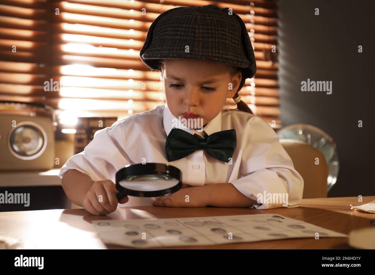 Joli petit détective explorant les empreintes digitales avec la loupe à la table dans le bureau Banque D'Images