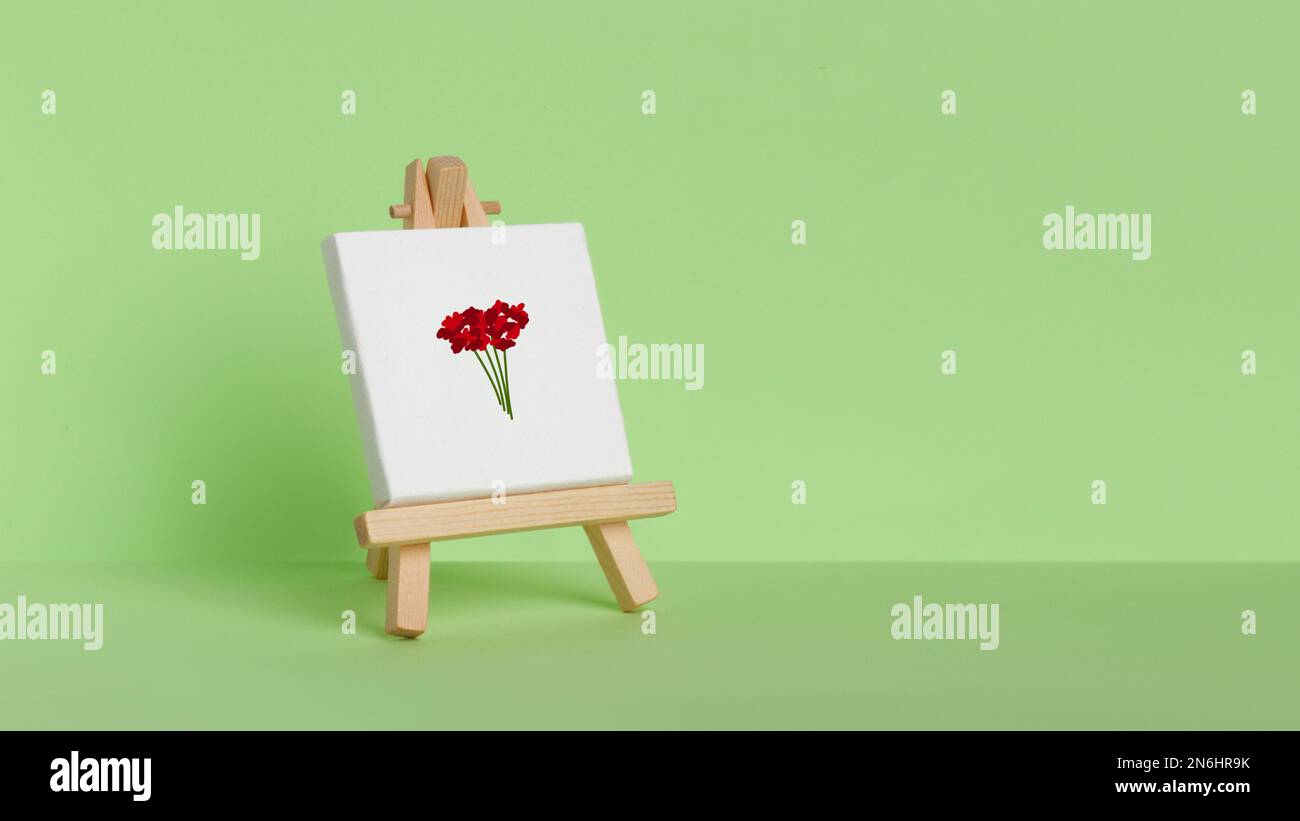 Mini-peinture sur un chevalet sur fond vert. Peint avec des fleurs rouges Banque D'Images