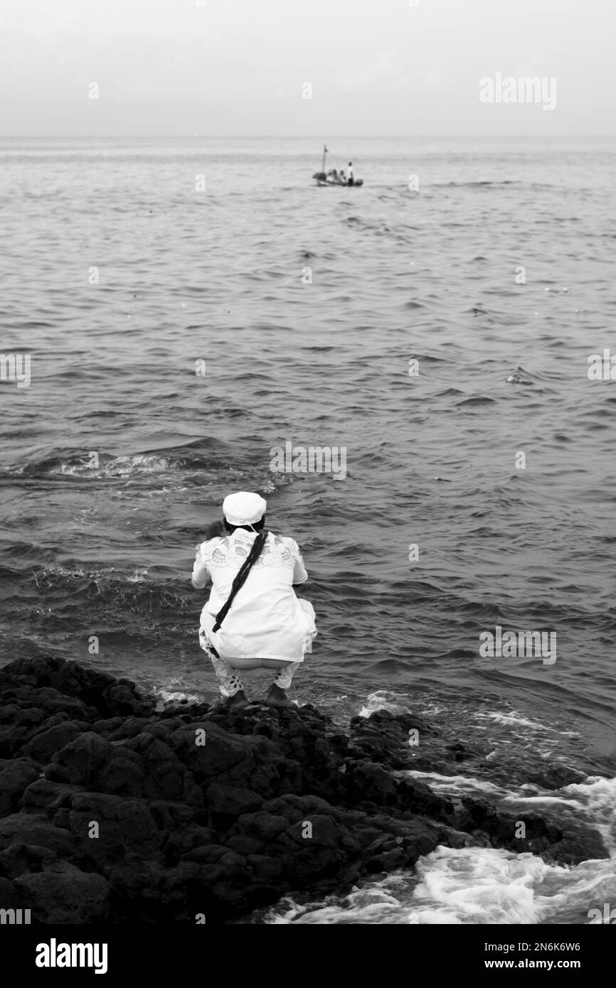 Salvador, Bahia, Brésil - 02 février 2017: Un homme jette des fleurs à Iemanja à partir d'un rocher sur la Reine de la mer Journée religieuse à Salvador, Bahia. Banque D'Images