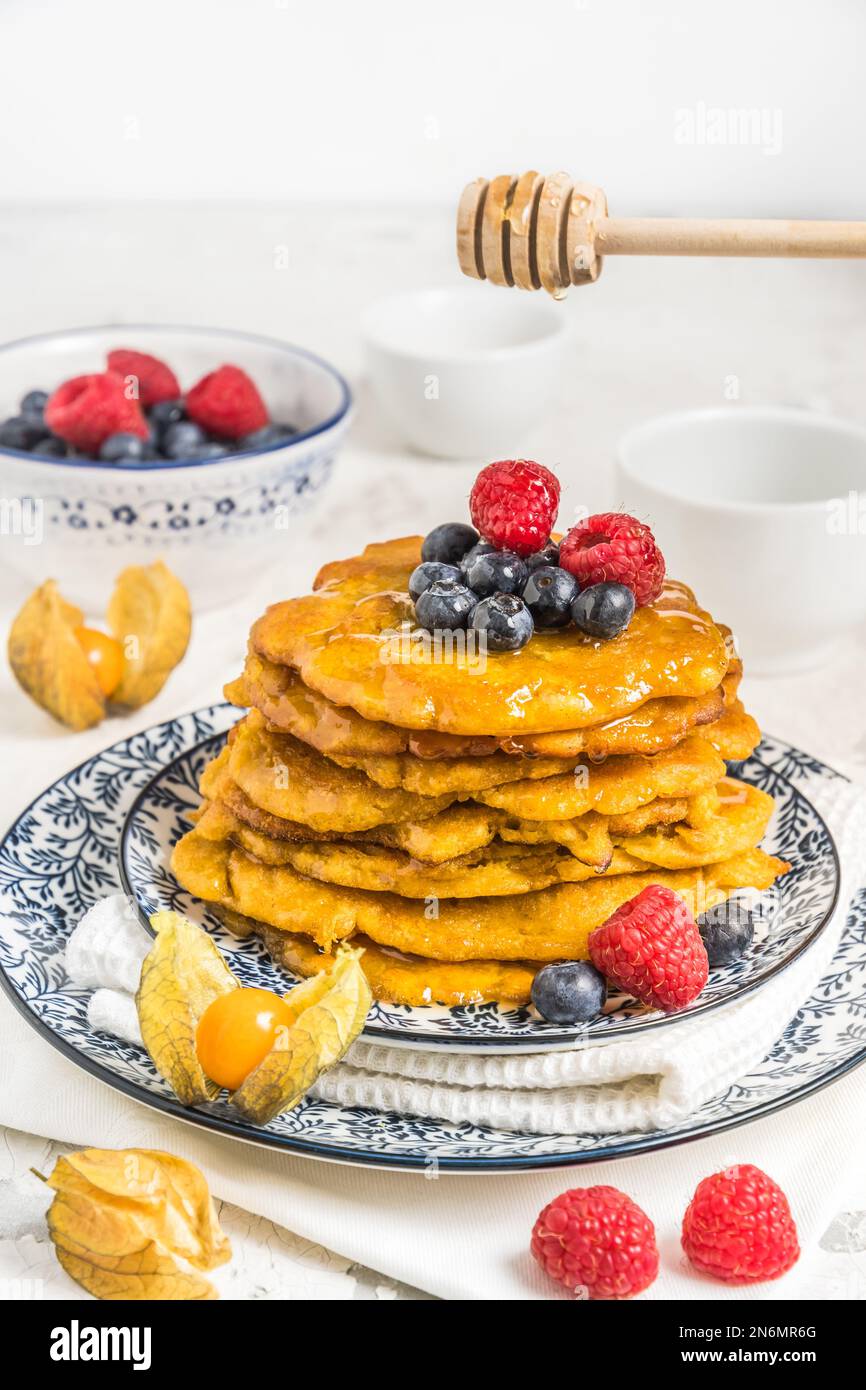 Pile de crêpes végétaliennes avec des baies et du sirop sur une assiette à motifs bleu-blanc sur fond blanc, verticale Banque D'Images