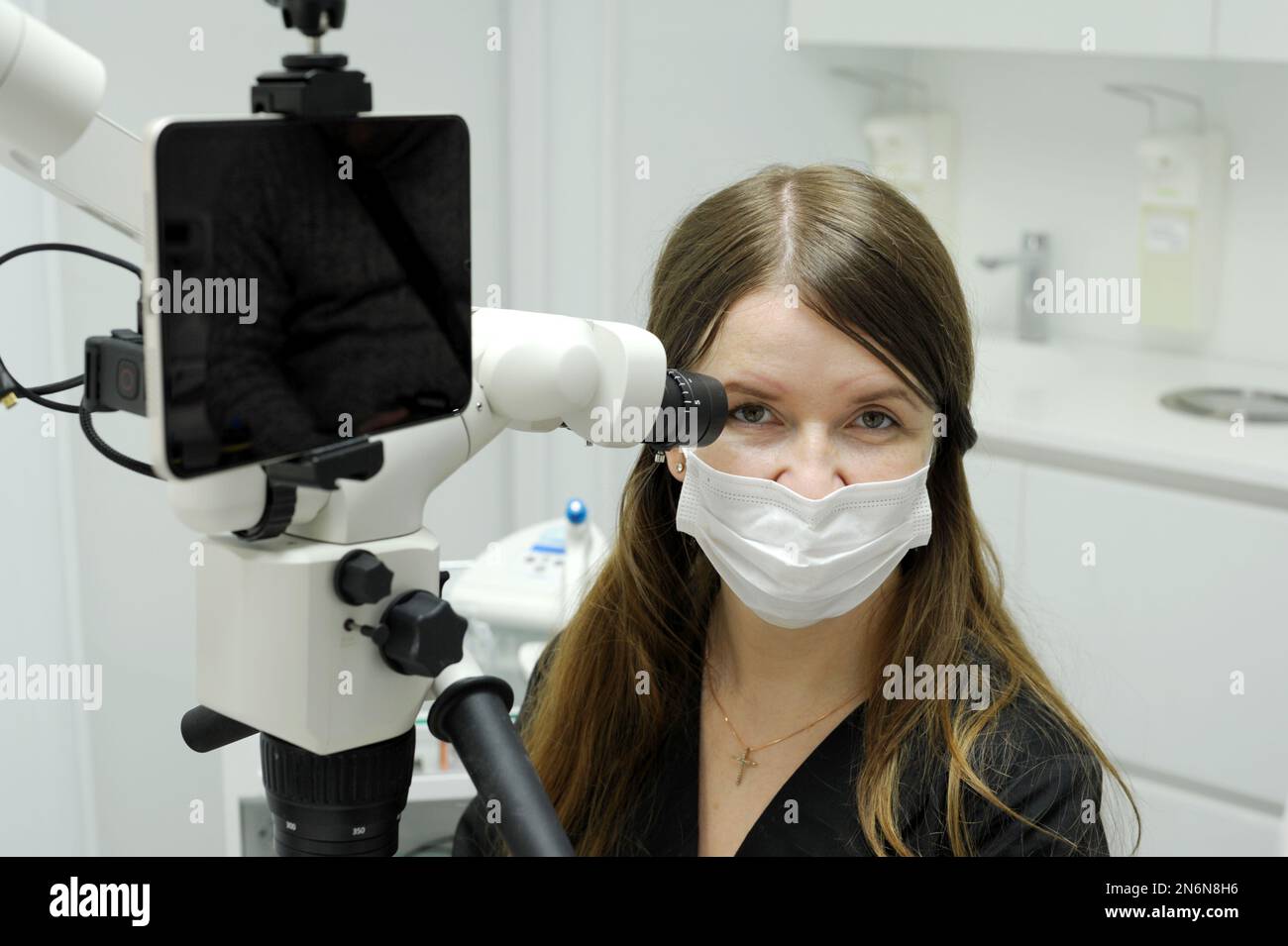 Tablette grand écran le jeune dentiste est assis près d'un microscope pour la recherche de traitement dentaire prothèses remplissant les canaux dents regarde dans le cadre un advertisem Banque D'Images