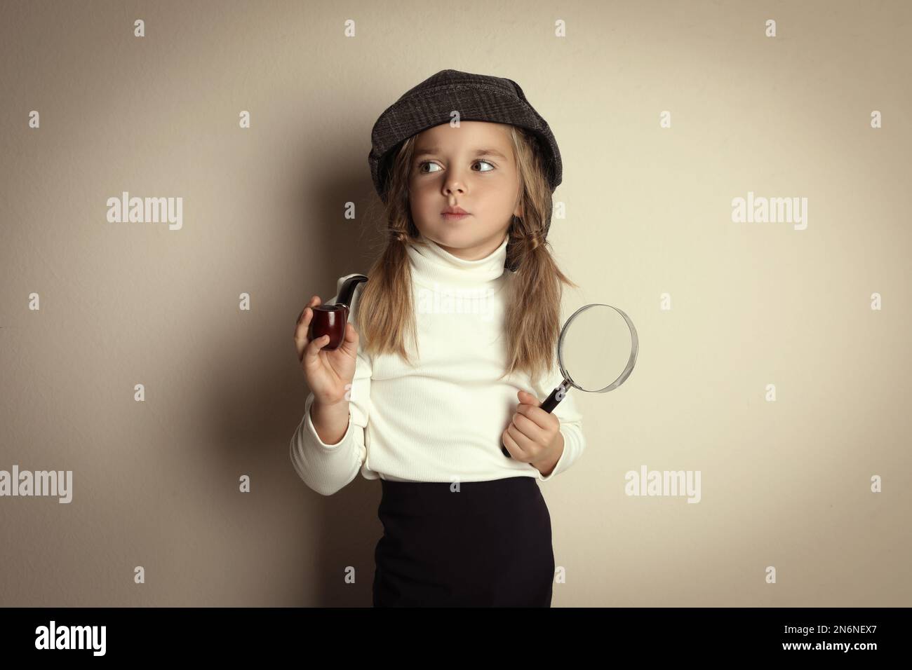 Joli petit enfant dans un chapeau avec pipe fumeur et loupe jouant détective sur fond beige Banque D'Images