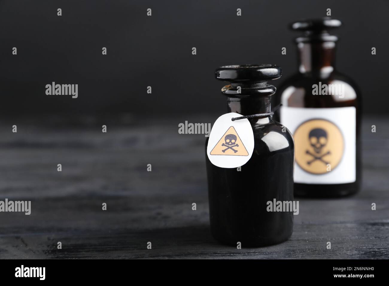 Bouteilles de poison en verre avec panneaux d'avertissement sur table en bois noir. Espace pour le texte Banque D'Images