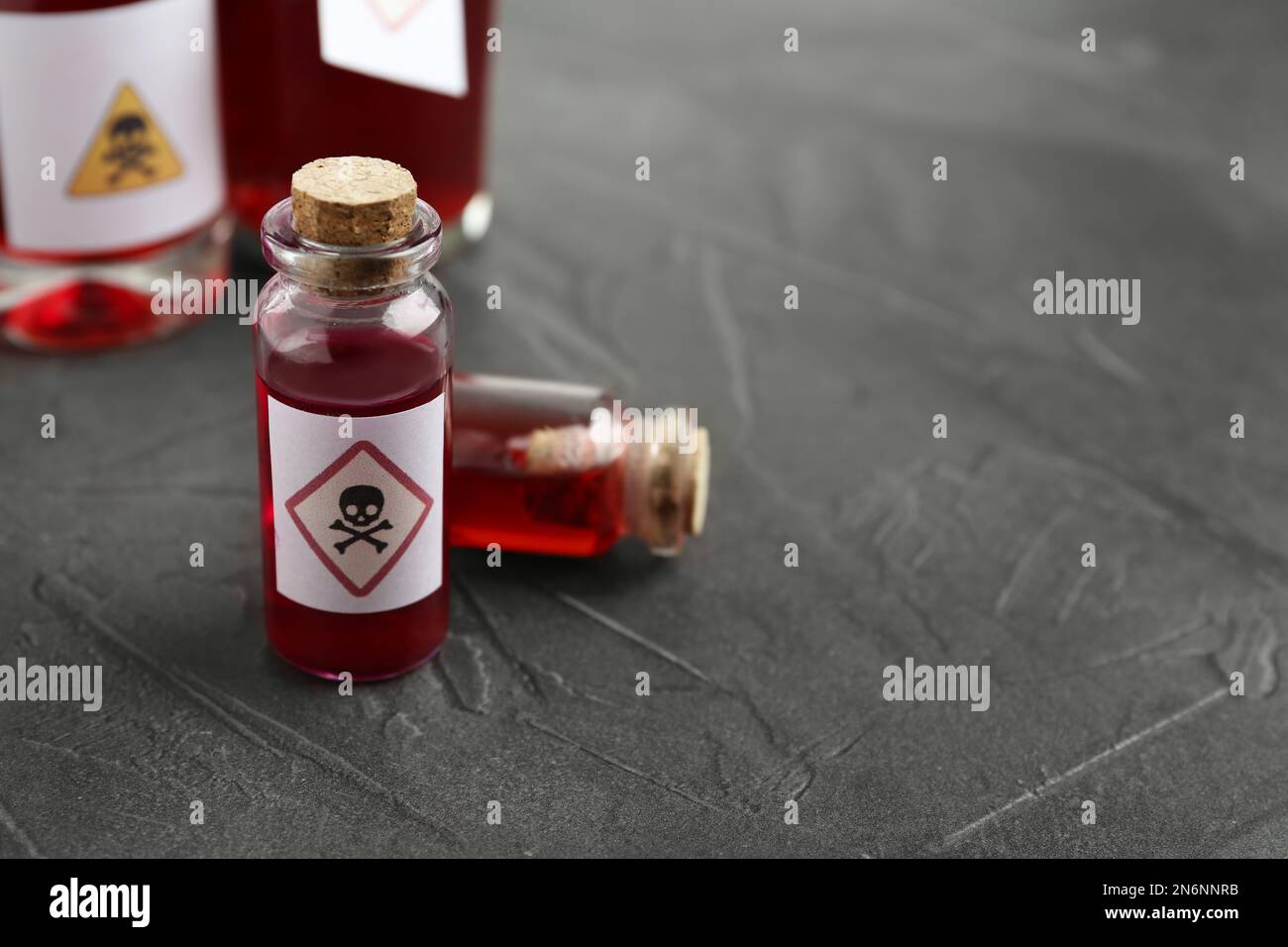 Flacons en verre de poison avec panneau d'avertissement sur la table en pierre grise, gros plan. Espace pour le texte Banque D'Images