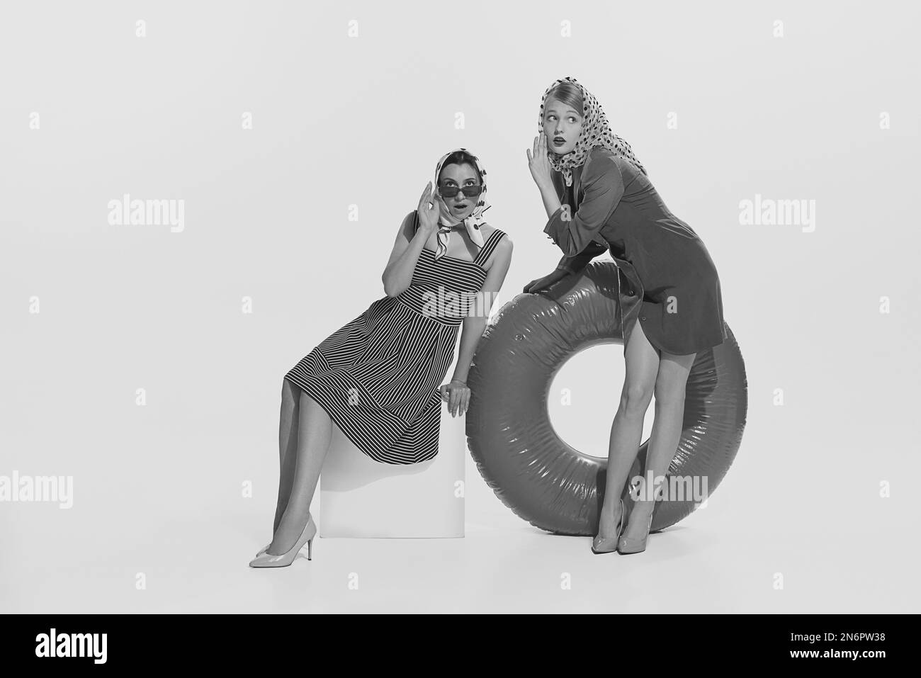 Portrait noir et blanc de deux jeunes femmes stylées en croisière assis chuchotant des commérages. Concept de mode vintage, Voyage, 70s, 80s style de mode Banque D'Images