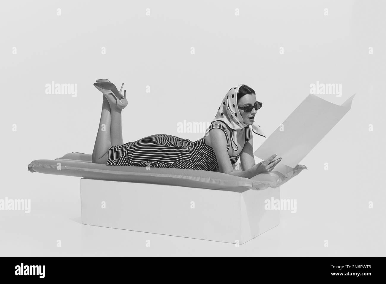 Portrait monochrome de jeune belle femme couché sur un matelas gonflable et magazine de lecture. Style rétro d'art vintage, mode 70s, 80s Banque D'Images