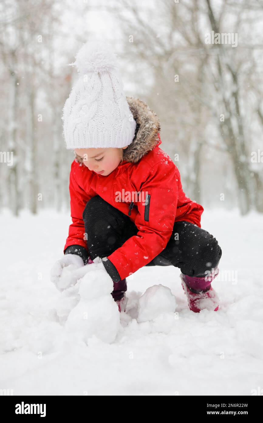 Jolie petite fille faisant des boules de neige à l'extérieur le jour de l'hiver Banque D'Images