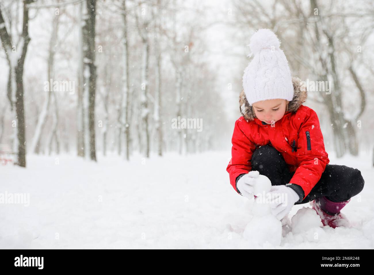 Jolie petite fille faisant des boules de neige à l'extérieur le jour de l'hiver, espace pour le texte Banque D'Images