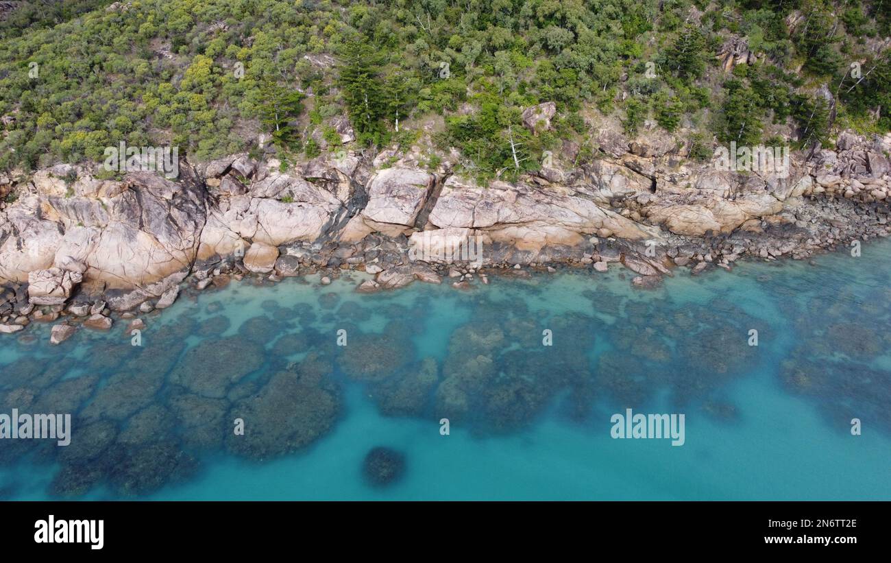 Image aérienne abstraite de l'eau claire et du récif contre une rive rocheuse avec des palmiers Banque D'Images