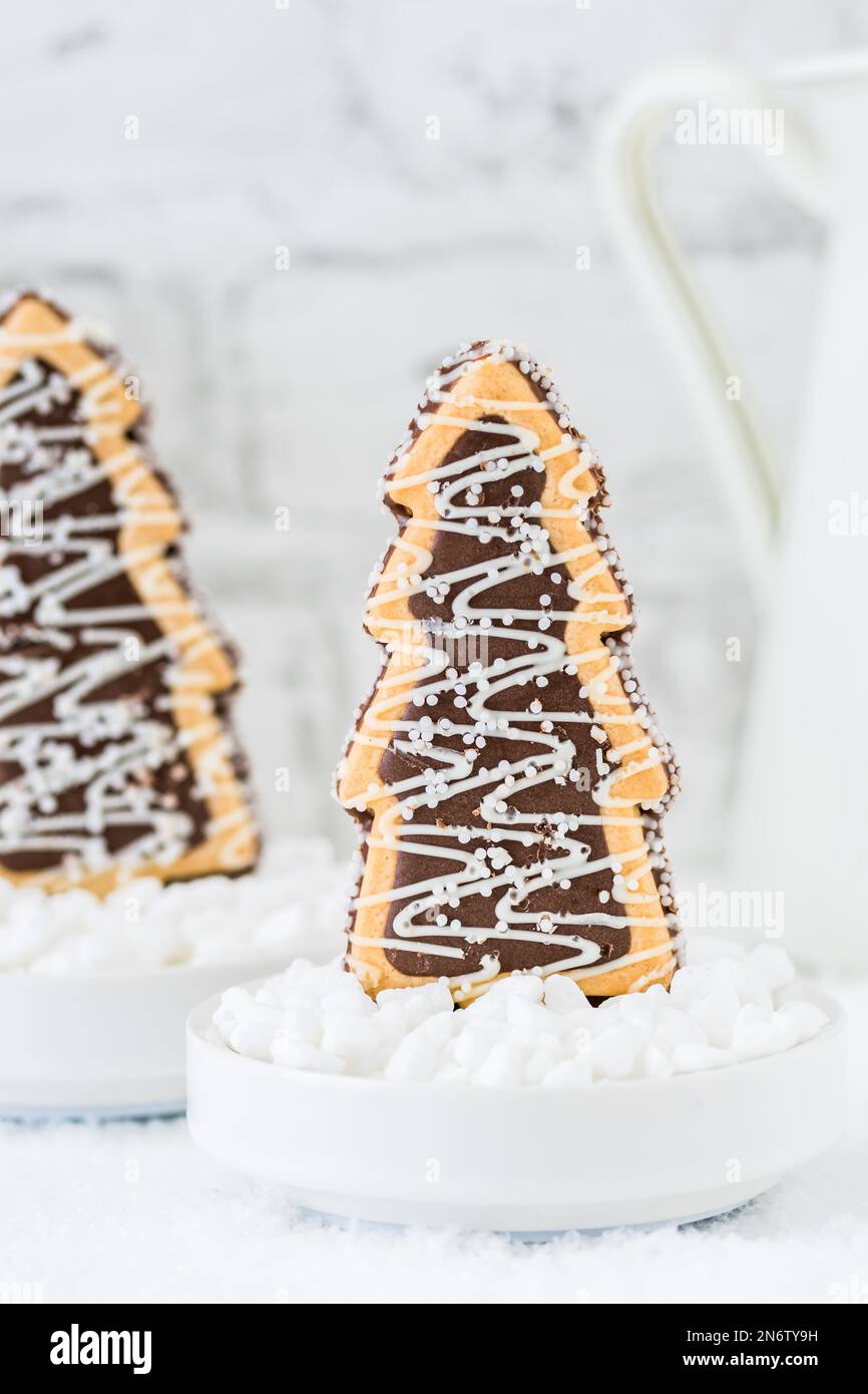 Deux biscuits en forme d'arbres de noël avec chocolat et sucre glacer dans des bols avec du sucre grossier sur fond blanc avec de la vaisselle blanche Banque D'Images