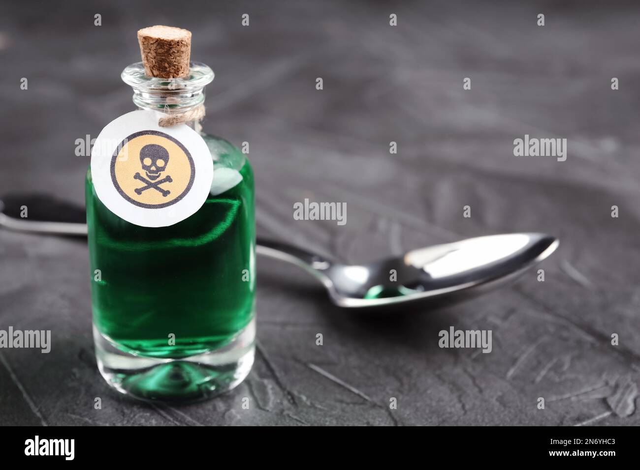 Bouteille de poison en verre avec panneau d'avertissement et cuillère sur table en pierre grise, gros plan. Espace pour le texte Banque D'Images