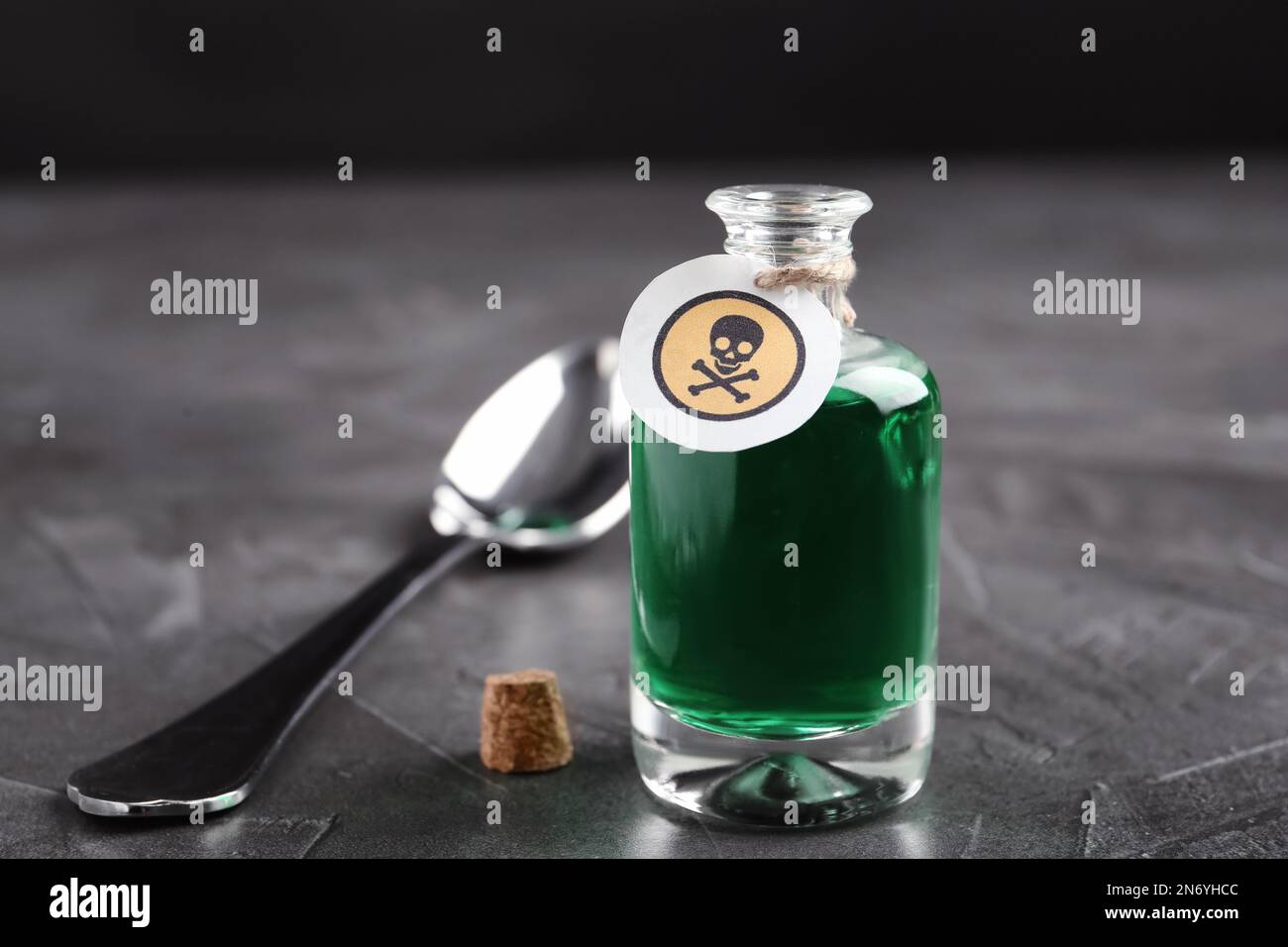 Bouteille de poison en verre avec panneau d'avertissement et cuillère sur table en pierre grise Banque D'Images
