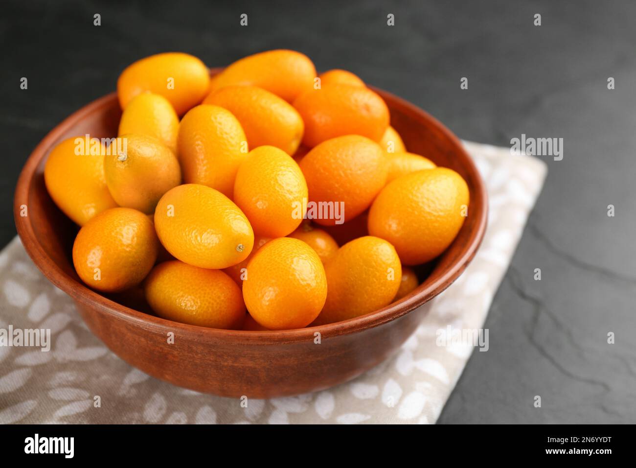 Kumquats mûrs frais dans un bol sur une table noire, gros plan Banque D'Images