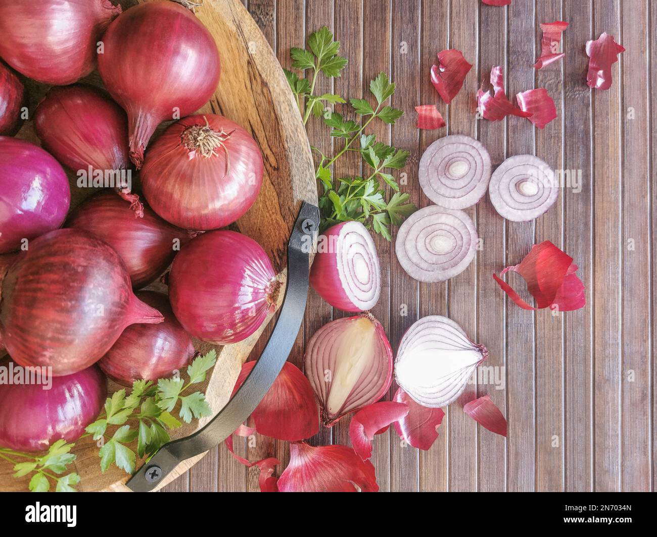 Photo composition vue avec des oignons entiers dans un bol traditionnel en bois, fond avec table en bois et tranches d'oignons et branche de persil... Banque D'Images