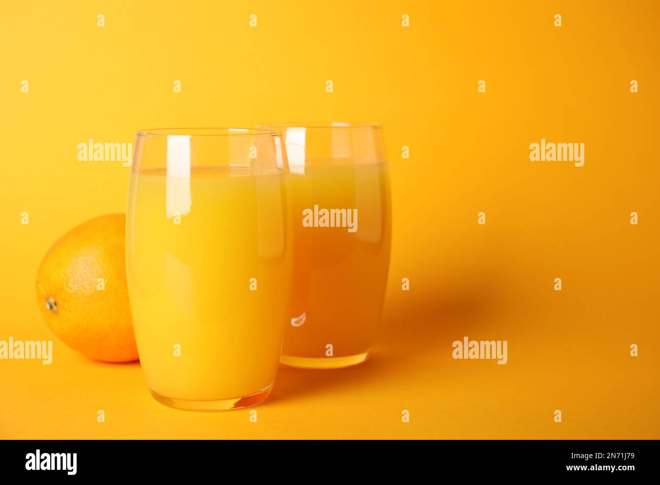 Jus d'orange fraîchement préparé dans des verres sur fond de couleur, espace pour le texte Banque D'Images