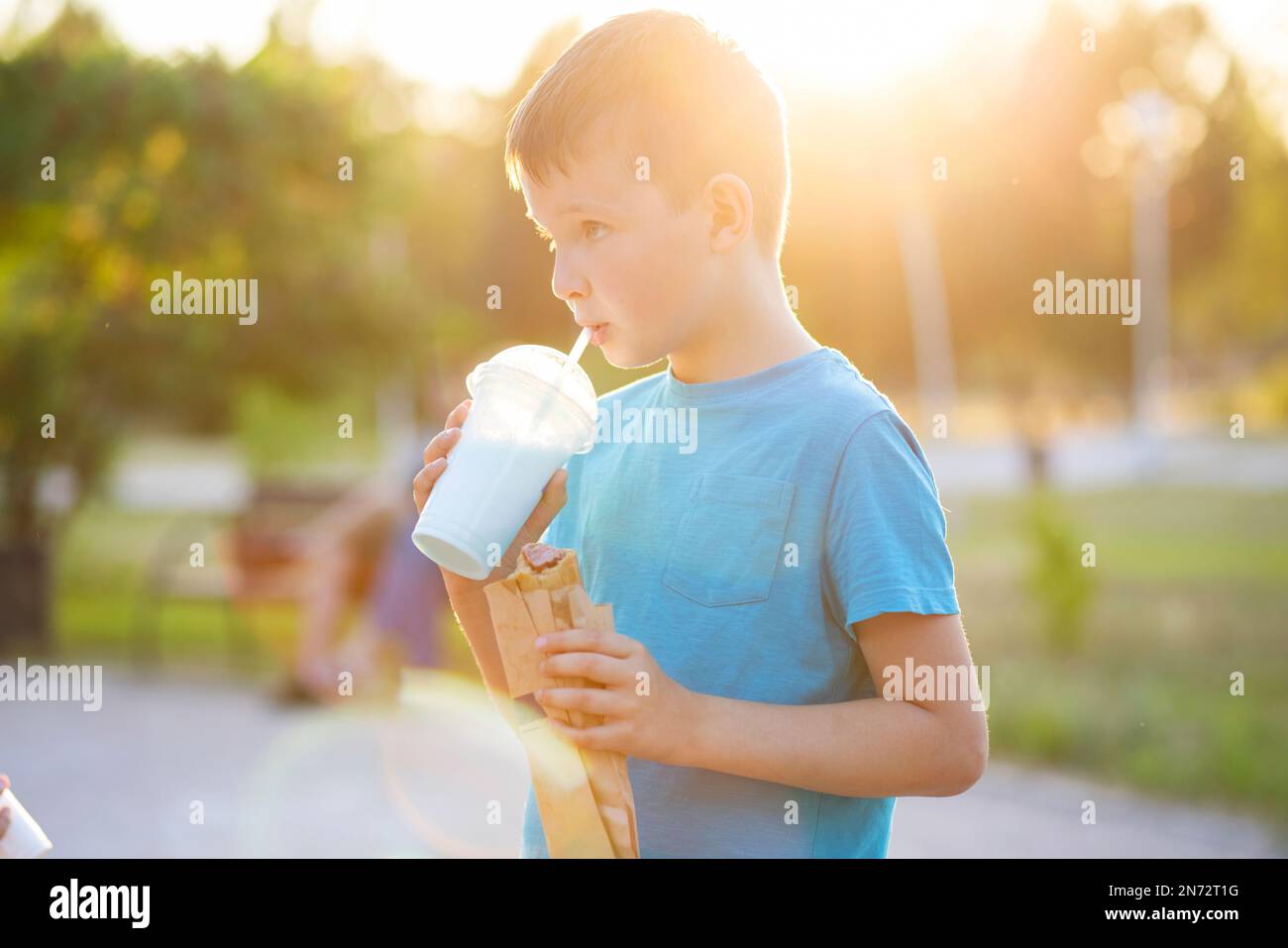 Un enfant boit un milk-shake et mange un hot dog à l'extérieur dans un parc Banque D'Images