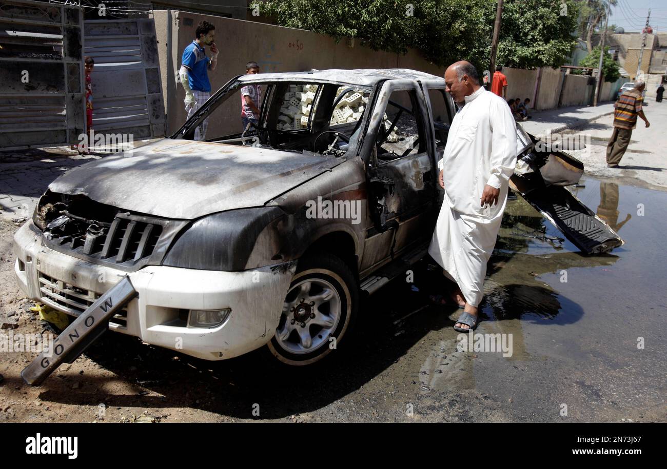 Civilians inspect the aftermath of a car bomb attack in Baghdad, Iraq, Wednesday, July 24, 2013. A bomb exploded near a Sunni mosque in Baghdad's southern Dora neighborhood on Tuesday killing several people and wounding many, police said. (AP Photo/Karim Kadim) Banque D'Images