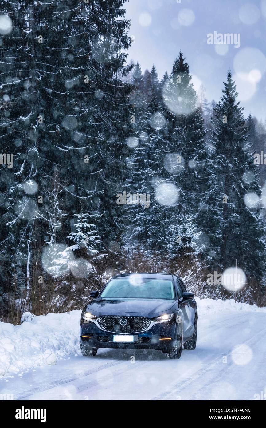 Italie, Vénétie, Belluno, une Mazda Motor Corp Véhicule utilitaire sport multisegment CX-30 (SUV) sur une route de montagne en hiver lors d'une chute de neige, les Dolomites Banque D'Images