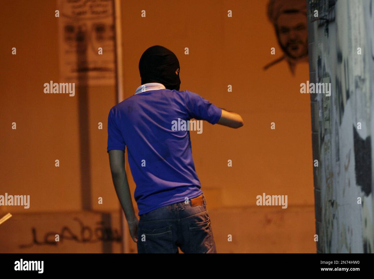 A masked Bahraini anti-government protester looks out for riot police during clashes in Bilad al-Qadeem, Bahrain, late Friday, July 19, 2013. Nightly protests demanding democracy continued in villages across the Gulf island kingdom. Graffiti on the wall, lower left, reads: "Down Hamad" referring to Bahrain's king. (AP Photo/Hasan Jamali) Banque D'Images
