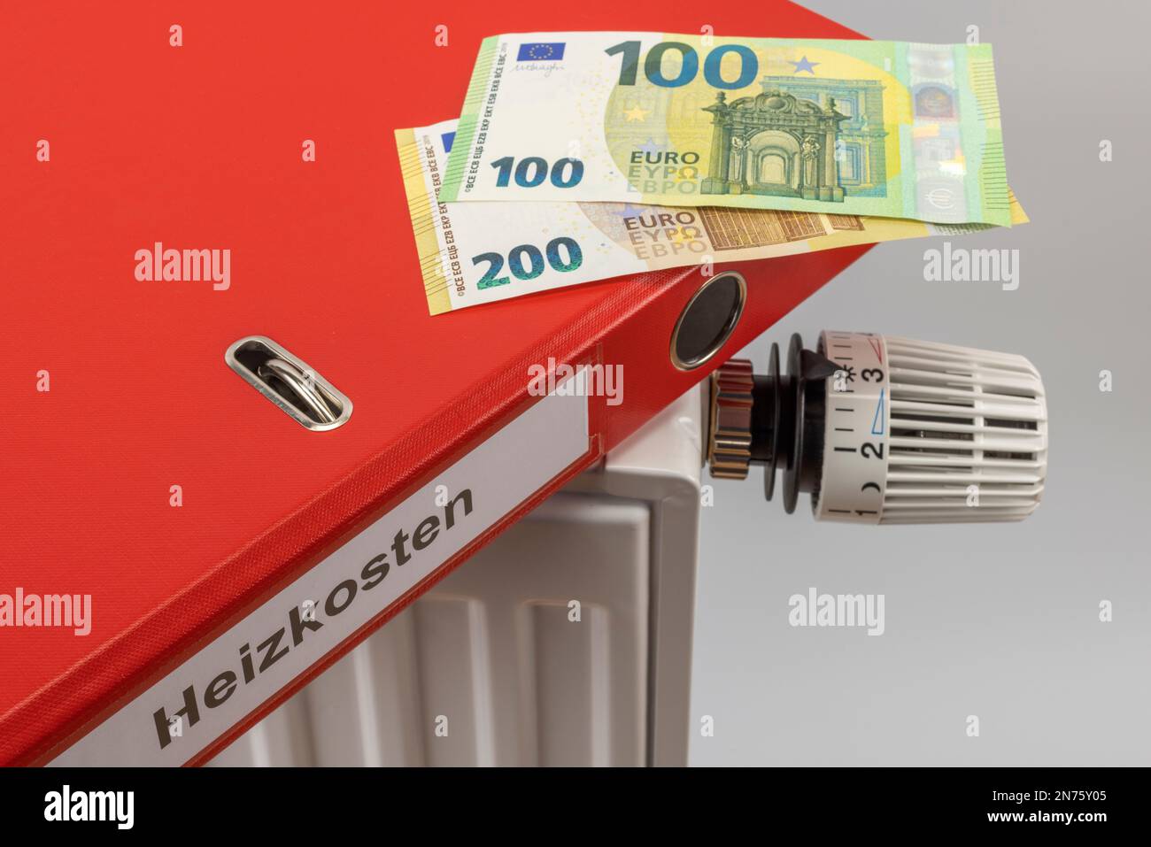Dossier rouge avec les coûts de chauffage des étiquettes, les factures en euros se trouvent sur le radiateur, image de symbole, taux d'énergie fixe de 300 euros, coûts d'énergie, augmentation des coûts de chauffage, fond blanc, Banque D'Images