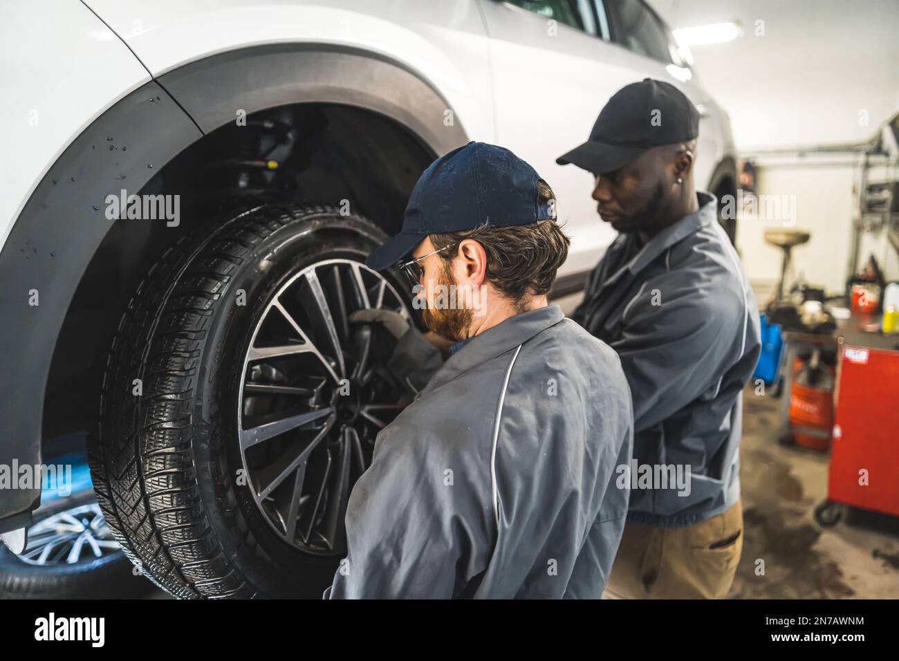 vue arrière moyenne de deux mécaniciens changeant la roue sur une voiture, atelier de réparation de voiture. Photo de haute qualité Banque D'Images