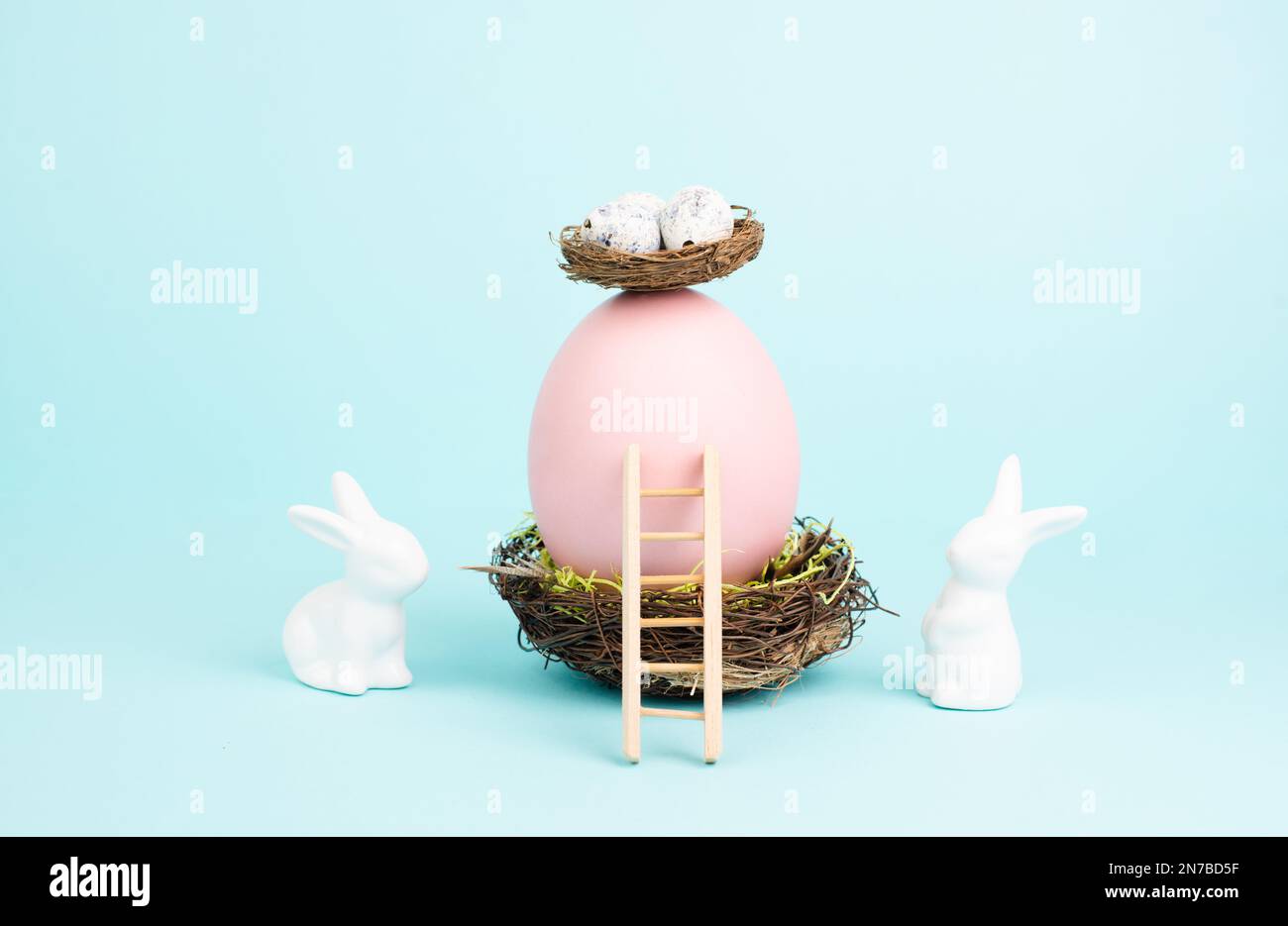 Lapin ou lapin de Pâques assis à côté d'un énorme œuf de couleur rose dans un nid d'oiseaux, ruban cadeau et échelle, vacances de printemps Banque D'Images