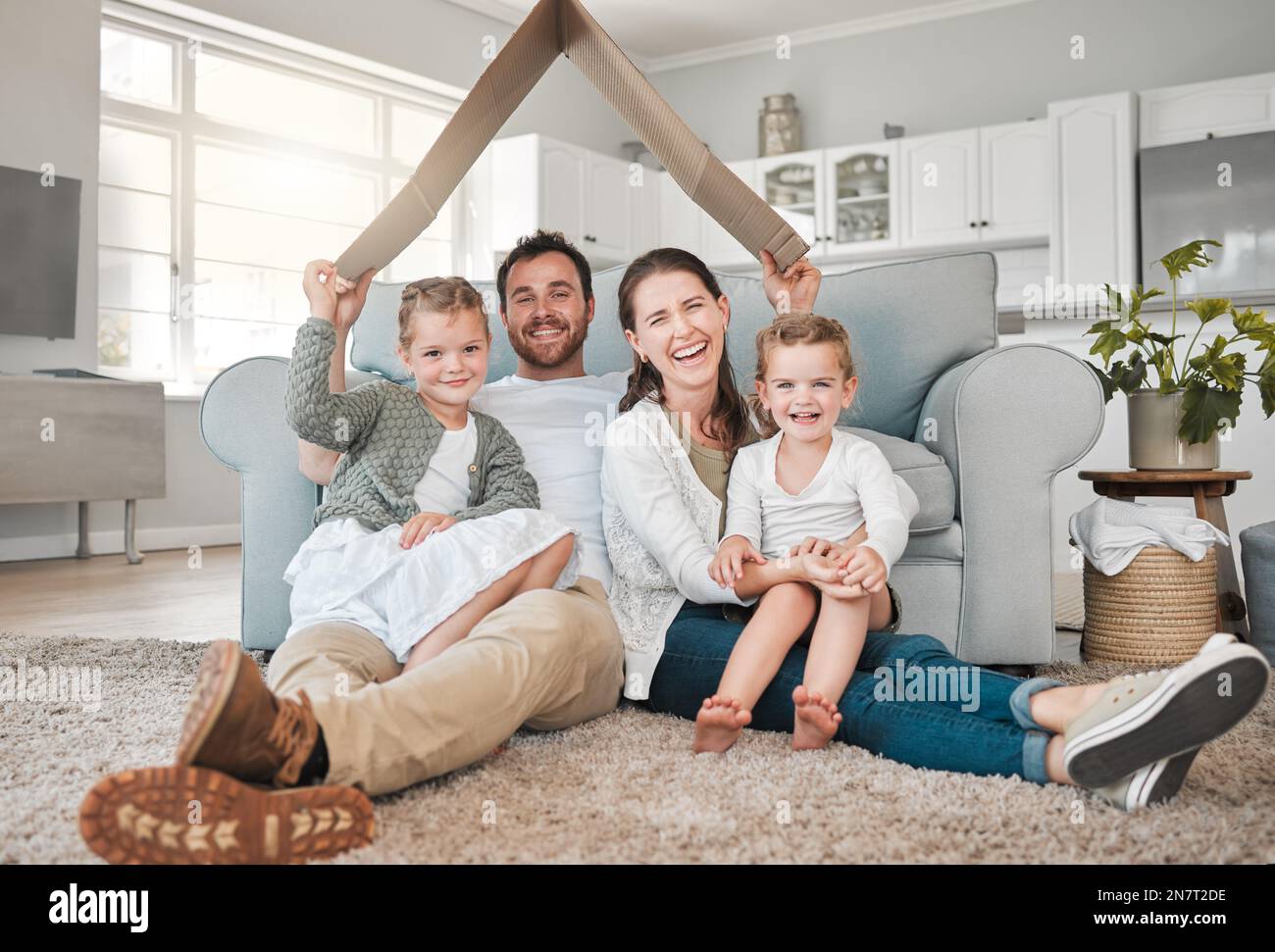 La maison est là où vous êtes aimés. Portrait d'une jeune famille assise sur le plancher du salon sous un fort en carton à la maison. Banque D'Images
