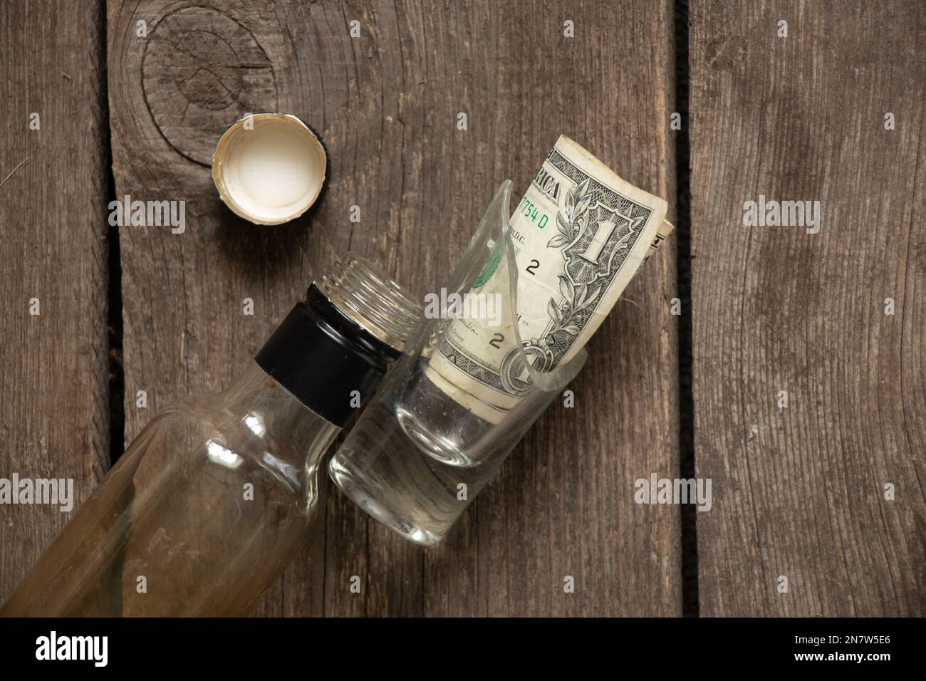dollars américains dans un verre et à côté d'une bouteille vide sur une vieille table en bois, dépendance à l'alcool Banque D'Images