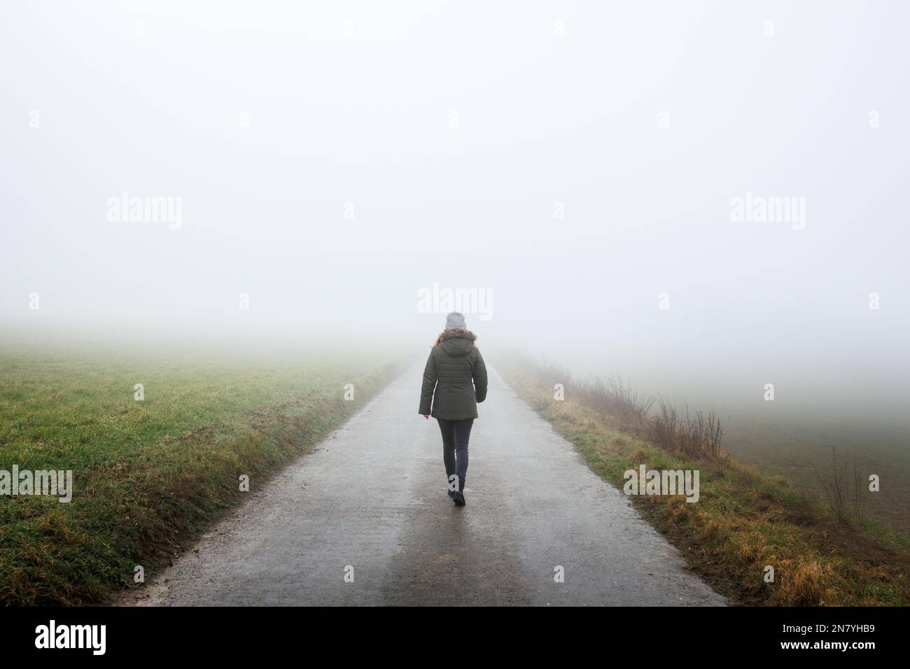 Une femme solitaire marche sur une route vide dans le brouillard. Voyage vers un endroit inconnu. Solitude femme marchant à l'extérieur Banque D'Images