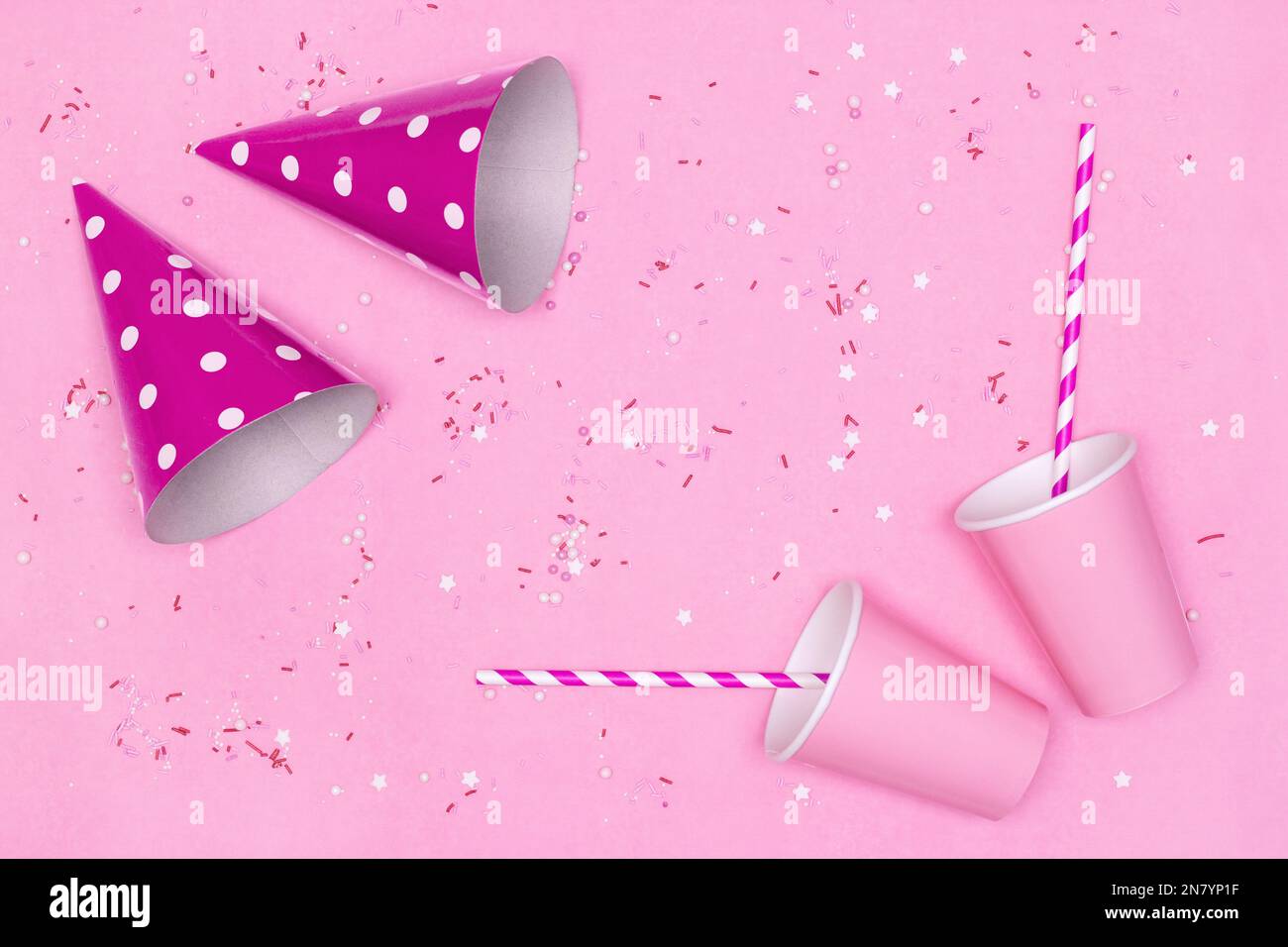 Gobelets en papier, pailles à boire à rayures, chapeaux de fête avec bonbons saupoudrées sur fond rose. Concept fête d'anniversaire. Copier l'espace Banque D'Images