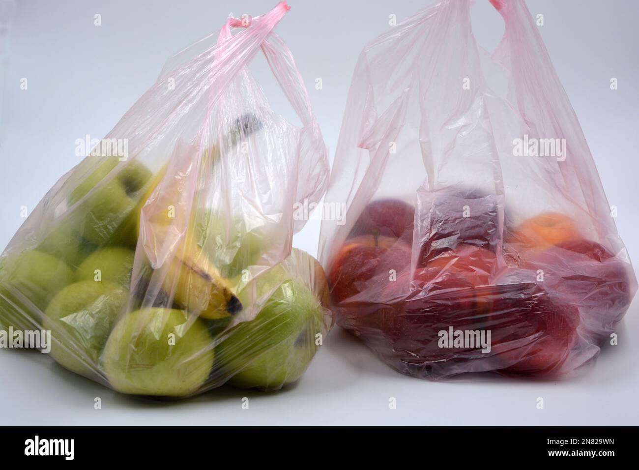 Deux grands paquets de fruits, des aliments sains, beaucoup de pommes rouges mûres et des pommes vertes avec une banane mûre se trouvent dans des sacs jetables roses. Banque D'Images