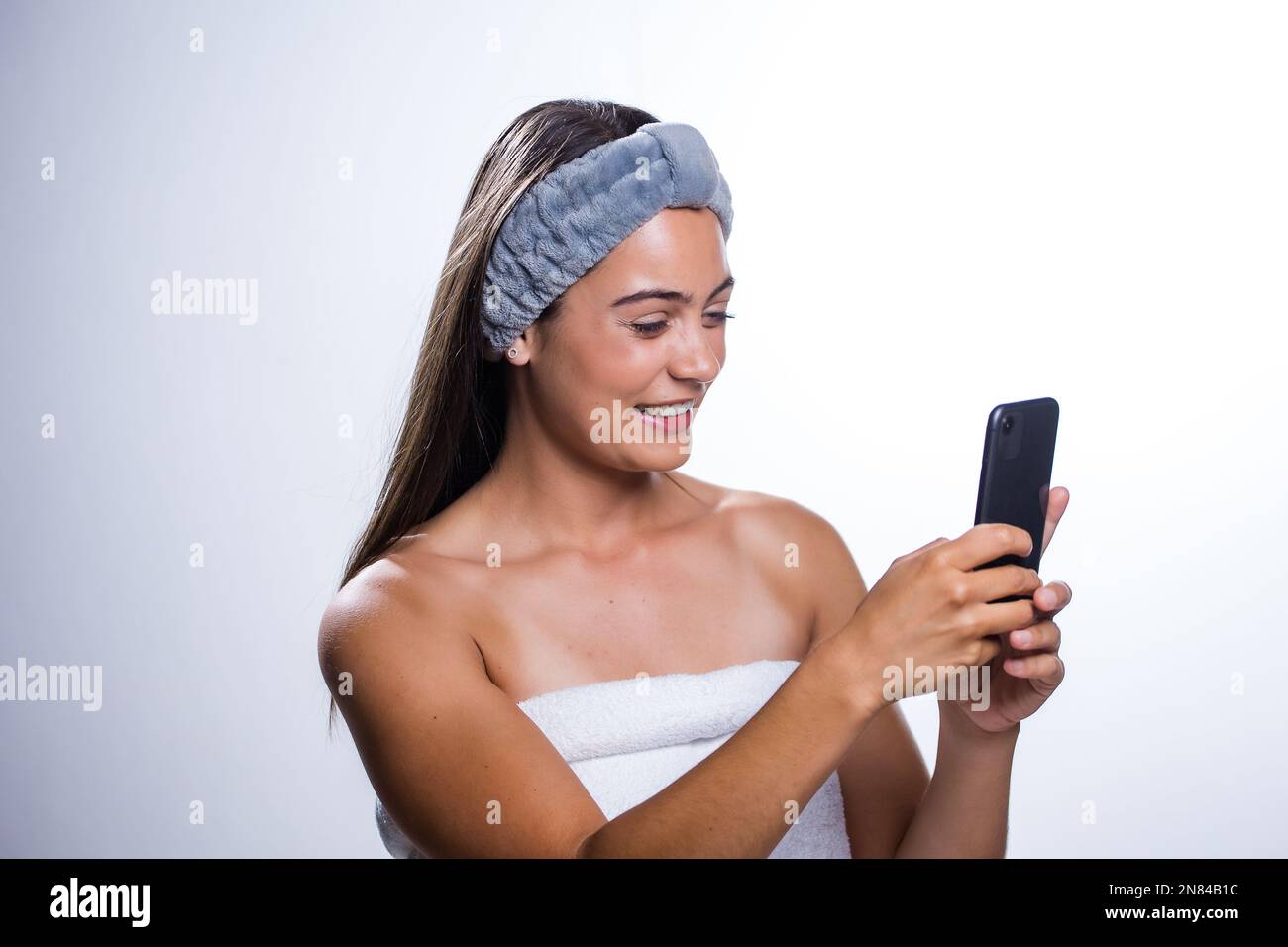 Une femme de race blanche heureuse avec un bandeau de serviette et une  serviette de bain enveloppée autour de sa poitrine, tenant et regardant le  mobile Photo Stock - Alamy