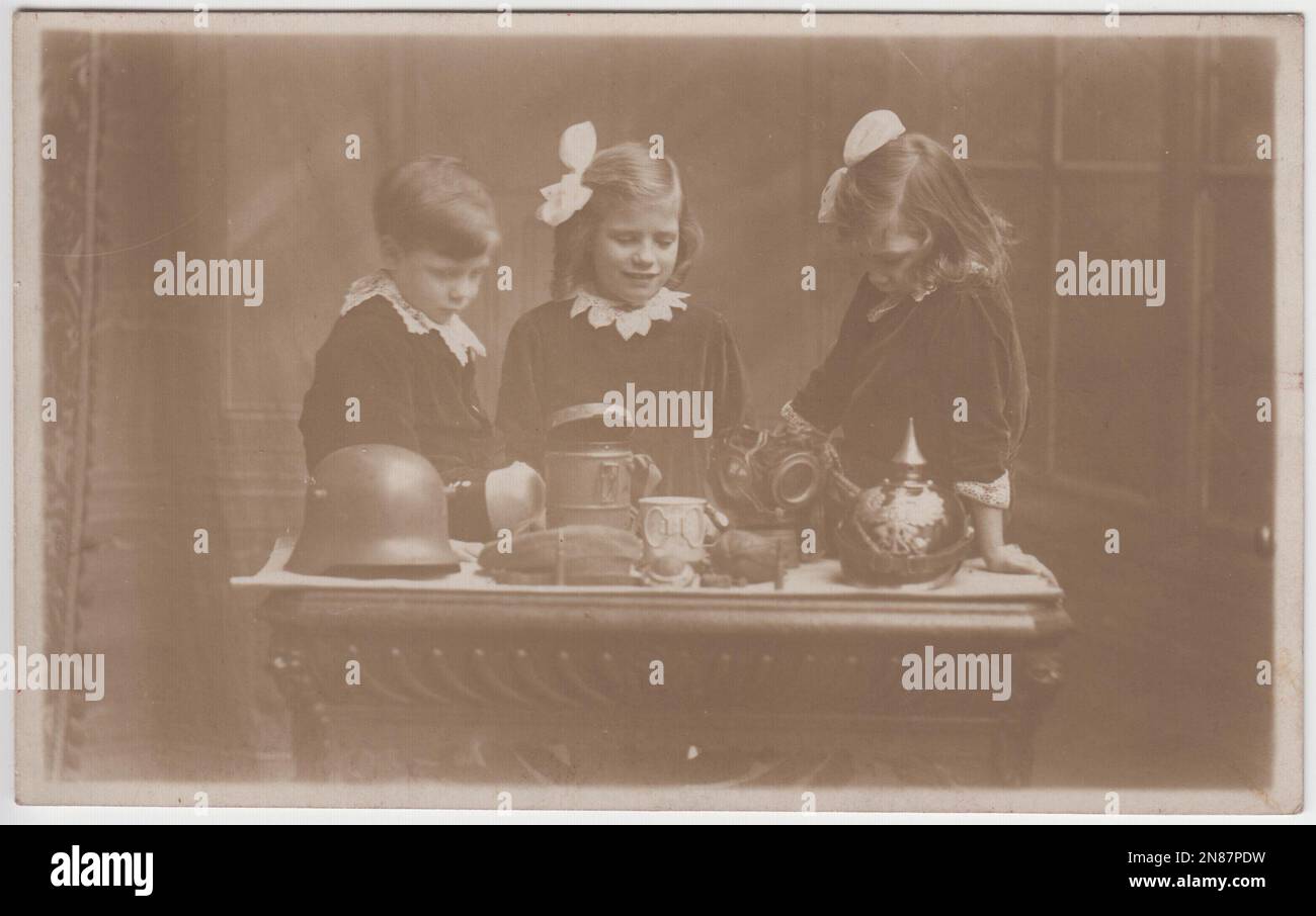 Trois jeunes enfants britanniques regardant les trophées de la première Guerre mondiale tirés de soldats allemands. Les objets disposés sur la table comprennent un casque allemand Pickelhaube, un casque Stahlhelm, un cache-champ, un masque à gaz et une tasse ou une tasse en étain. La photo a été prise par les Tasma Studios, 99 Wellington Street, Woolwich, Londres Banque D'Images