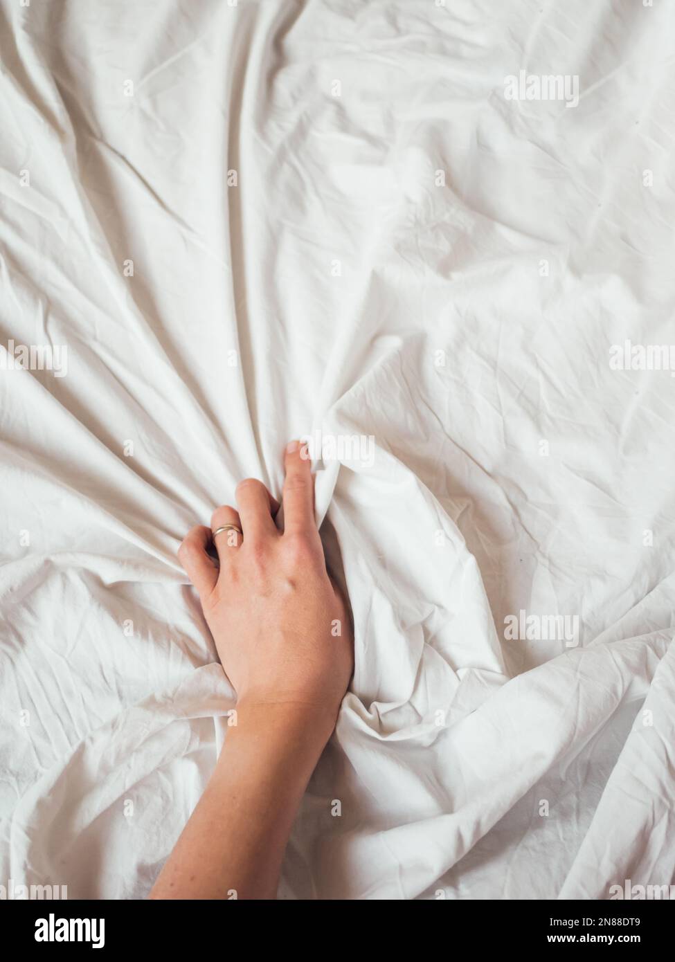 Main de femme sur fond de drap de lit froissé. Lit non fait froissé. La femme presse le linge blanc. Maison confortable et imparfaite. Maison confortable non idéale. Banque D'Images