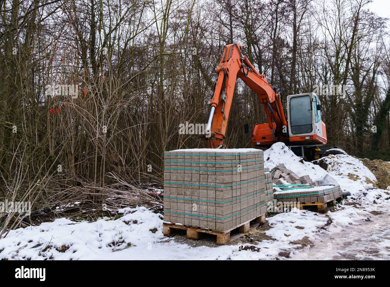 Palette en bois avec carrelages routiers et pelle hydraulique sur un chantier enneigé Banque D'Images