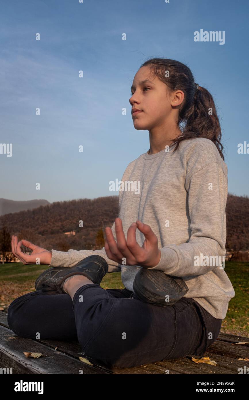 Une adolescente fait de l'exercice à l'extérieur et pratique des exercices de yoga dans le parc, assise sur une table en bois. Jeune femme trouvant sa paix intérieure. Banque D'Images