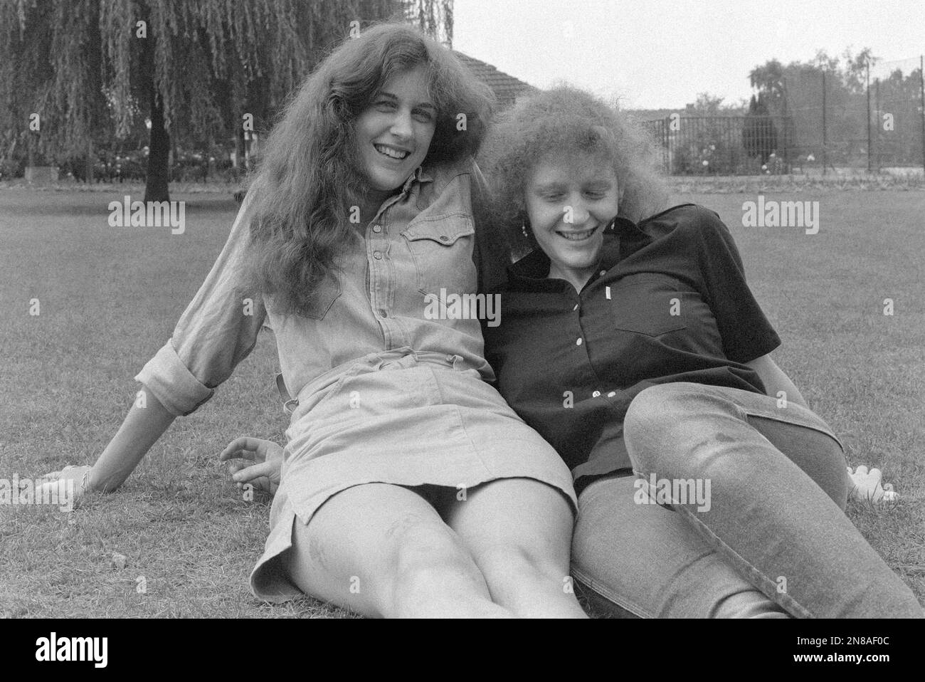 deux jeunes femmes se trouvant dans le parc public sur l'herbe fraîchement coupée appréciant la détente chaude journée d'été 1980s angleterre royaume-uni Banque D'Images